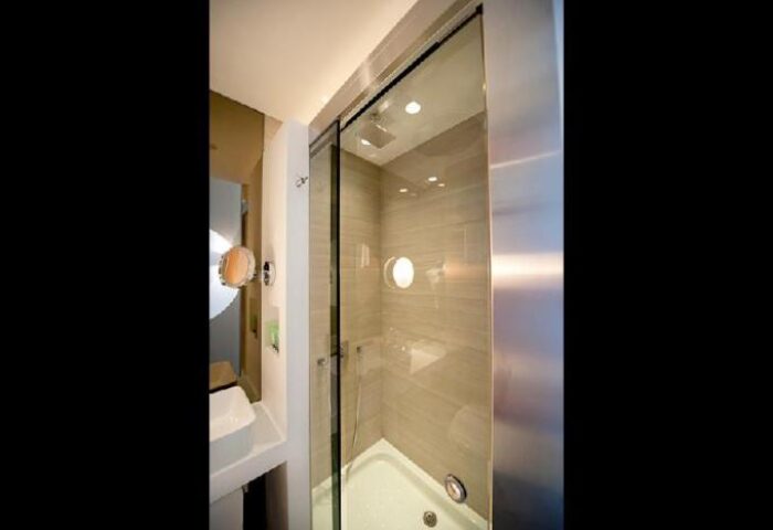 Shower in The Sheung Wan, a gay-friendly hotel. Modern bathroom with glass shower doors, round window, and sleek design. Ideal for gay travel.