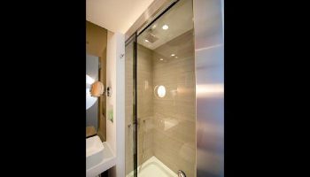 Shower in The Sheung Wan, a gay-friendly hotel. Modern bathroom with glass shower doors, round window, and sleek design. Ideal for gay travel.