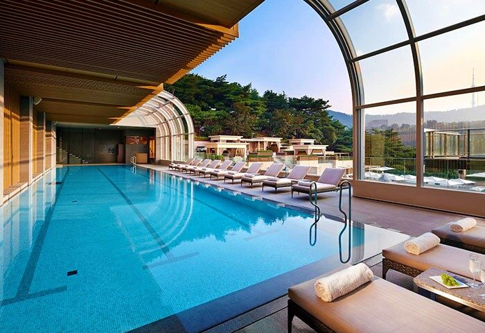 The Shilla Seoul gay-friendly hotel's indoor pool. Loungers line the pool with a view of the city. A luxury travel destination.