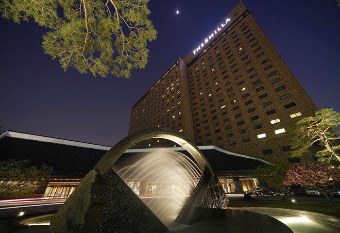 The Shilla Seoul hotel exterior at night. Gay-friendly hotel with fountain, modern architecture, and illuminated windows. Luxury travel in Seoul.