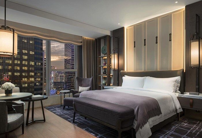 Hotel room at The St. Regis Hong Kong, a gay-friendly hotel. Bedroom with city view, bed, table, and chair. Luxury travel for gay men.