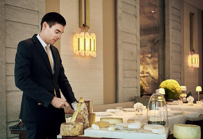 The St. Regis Hong Kong, gay-friendly hotel. Waiter cuts cheese at a table in a luxury restaurant. Fine dining experience for gay travelers.