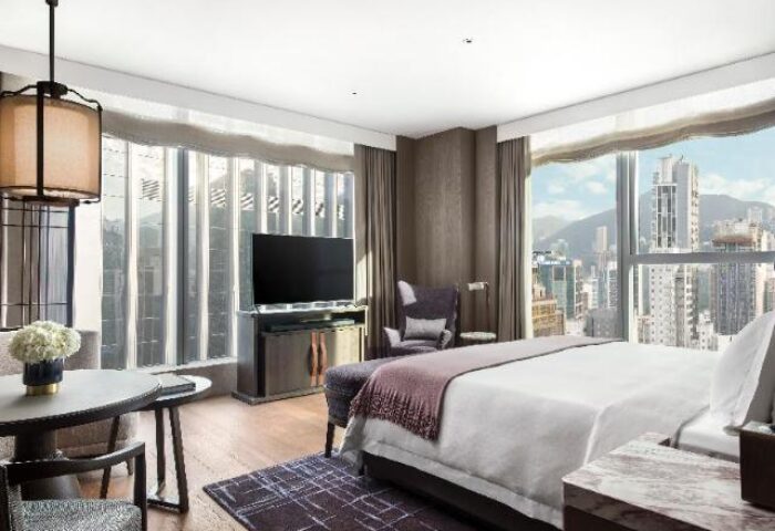St. Regis Hong Kong hotel room. Modern design, city view. Gay-friendly travel destination. Luxurious bedding, TV, and stylish decor.