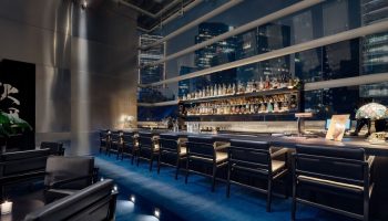 Bar at The St. Regis Mexico City, a gay-friendly hotel. Night cityscape view. Upscale bar with blue carpet, black chairs, and liquor.