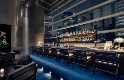 Bar at The St. Regis Mexico City, a gay-friendly hotel. Night cityscape view. Upscale bar with blue carpet, black chairs, and liquor.