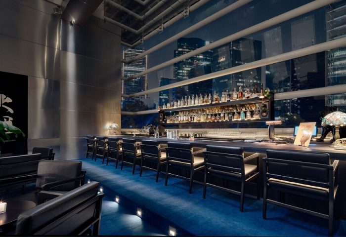 Bar at The St. Regis Mexico City, a gay-friendly hotel. Night cityscape view. Upscale bar with blue carpet, black chairs, and liquor.