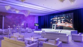 Event space at The St. Regis Mexico City, a gay-friendly hotel. Stage, white seating, and chandeliers under purple lighting.