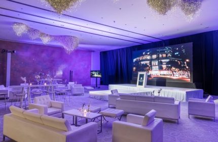 Event space at The St. Regis Mexico City, a gay-friendly hotel. Stage, white seating, and chandeliers under purple lighting.