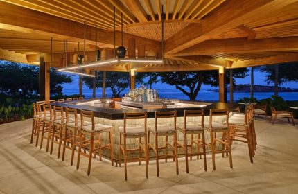 St. Regis Punta Mita Resort bar. Gay-friendly hotel with ocean view. Open-air bar, stools, wood beams, and bottles. Evening ambiance.