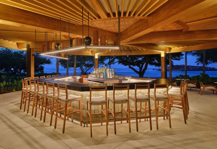 St. Regis Punta Mita Resort bar. Gay-friendly hotel with ocean view. Open-air bar, stools, wood beams, and bottles. Evening ambiance.