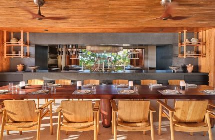 Dining area at The St. Regis Punta Mita Resort, a gay-friendly hotel. Long table set with plates and glasses, wooden chairs, and ceiling fans.