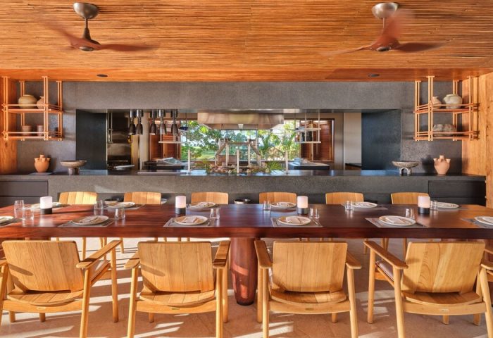 Dining area at The St. Regis Punta Mita Resort, a gay-friendly hotel. Long table set with plates and glasses, wooden chairs, and ceiling fans.