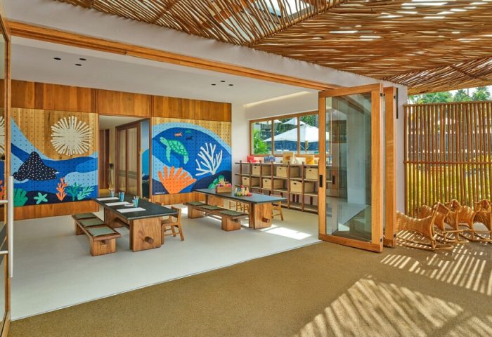 Playroom at The St. Regis Punta Mita Resort, a gay-friendly hotel. Kids' area with tables, benches, and colorful ocean-themed murals. Rattan ceiling.