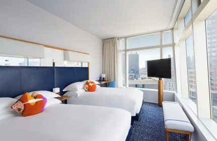 The Standard East Village hotel room. Gay-friendly lodging with two beds, colorful pillows, and a city view. Modern design for gay travel.