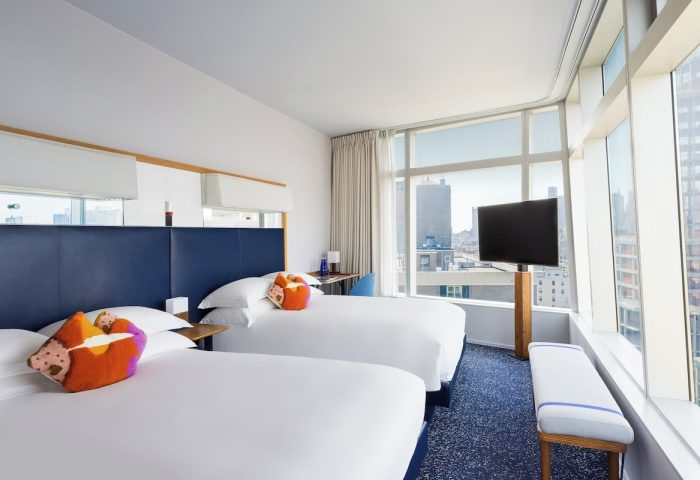 The Standard East Village hotel room. Gay-friendly lodging with two beds, colorful pillows, and a city view. Modern design for gay travel.