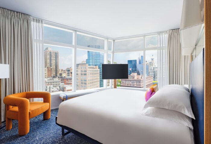 The Standard East Village hotel room. Gay-friendly hotel with city view, bed, chair, and TV. Great for gay travel in NYC.