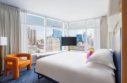 The Standard East Village hotel room. Gay-friendly hotel with city view, bed, chair, and TV. Great for gay travel in NYC.