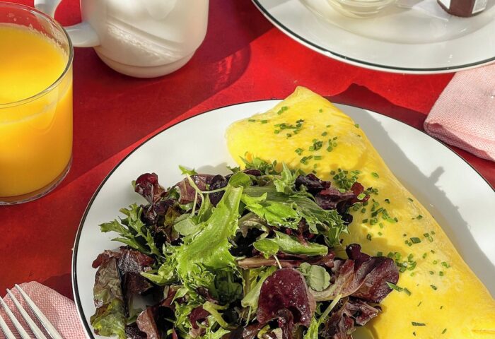 Breakfast at The Standard East Village, a gay-friendly hotel. Omelet, salad, croissant, coffee, and orange juice on a red table.