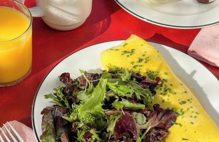 Breakfast at The Standard East Village, a gay-friendly hotel. Omelet, salad, croissant, coffee, and orange juice on a red table.