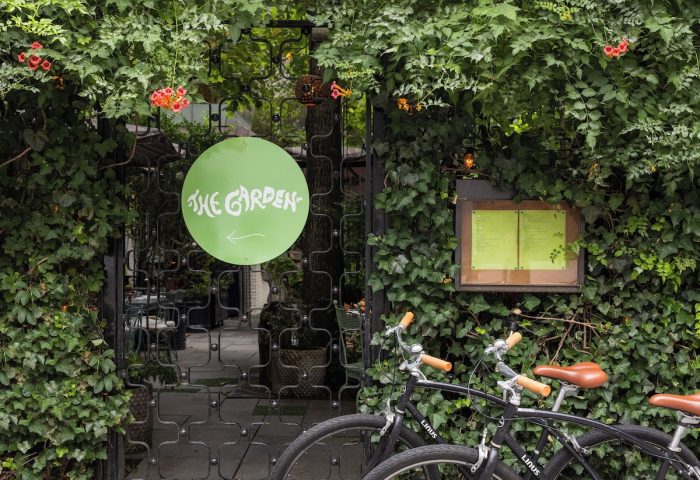 The Standard East Village hotel's entrance, a gay-friendly space. Bicycles parked outside The Garden sign, lush greenery surrounds the gate.