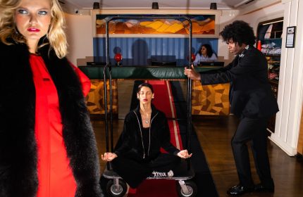 The Standard East Village, a gay-friendly hotel. Woman meditating on a luggage cart, pushed by a bellhop. Fashionable hotel lobby.