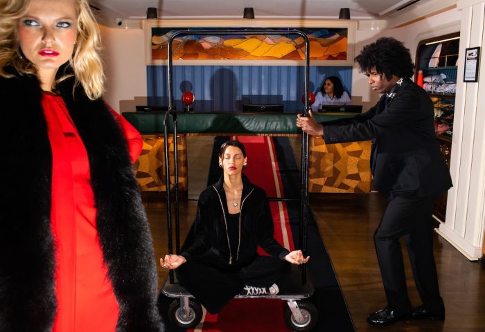 The Standard East Village, a gay-friendly hotel. Woman meditating on a luggage cart, pushed by a bellhop. Fashionable hotel lobby.