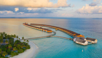 Aerial view of The Standard, Huruvalhi Maldives, a gay-friendly hotel. Overwater bungalows and turquoise waters. Tropical paradise.