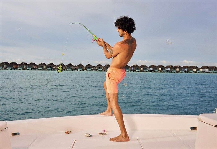 Gay man fishing at The Standard, Huruvalhi Maldives. Overwater bungalows in the background. Gay-friendly hotel. Maldives travel.