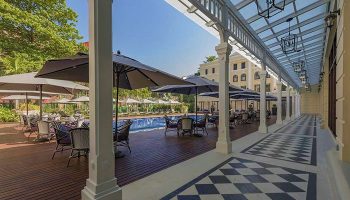 The Strand Yangon gay-friendly hotel. Poolside tables with umbrellas. Checkered floor and covered walkway. Luxury travel for gay men.