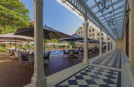 The Strand Yangon gay-friendly hotel. Poolside tables with umbrellas. Checkered floor and covered walkway. Luxury travel for gay men.