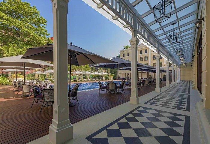 The Strand Yangon gay-friendly hotel. Poolside tables with umbrellas. Checkered floor and covered walkway. Luxury travel for gay men.
