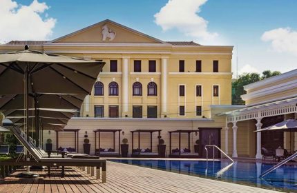 The Strand Yangon gay-friendly hotel pool. Loungers, umbrellas, and cabanas line the pool's edge. Yellow building in the background.
