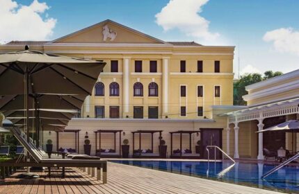 The Strand Yangon gay-friendly hotel pool. Loungers, umbrellas, and cabanas line the pool's edge. Yellow building in the background.