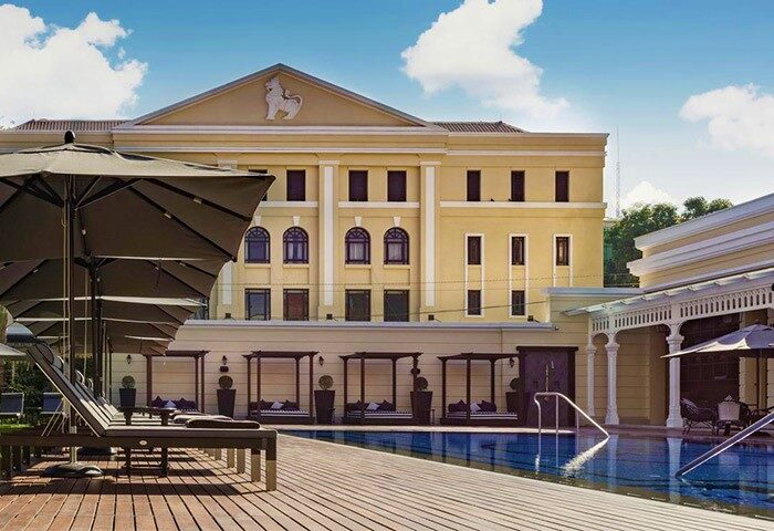 The Strand Yangon gay-friendly hotel pool. Loungers, umbrellas, and cabanas line the pool's edge. Yellow building in the background.