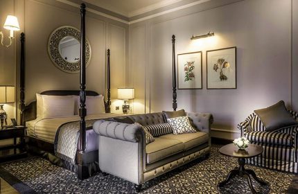 Gay-Friendly Hotel The Strand Yangon: Elegant room with four-poster bed, sofa, and armchair. A luxurious stay in Yangon, Myanmar.