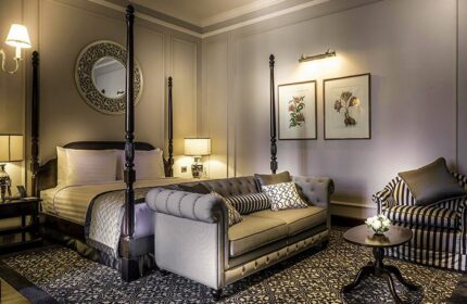 Gay-Friendly Hotel The Strand Yangon: Elegant room with four-poster bed, sofa, and armchair. A luxurious stay in Yangon, Myanmar.
