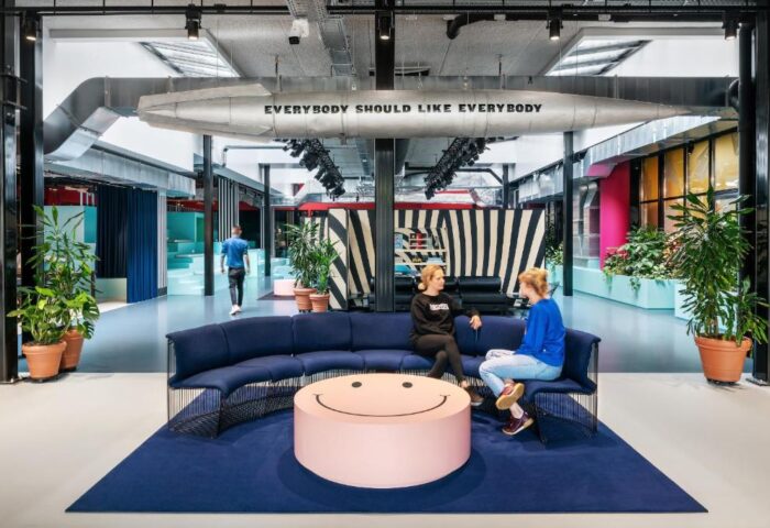The Student Hotel Amsterdam City lobby. Gay-friendly hotel with a modern design, featuring a lounge area with a smiley face table and colorful decor.