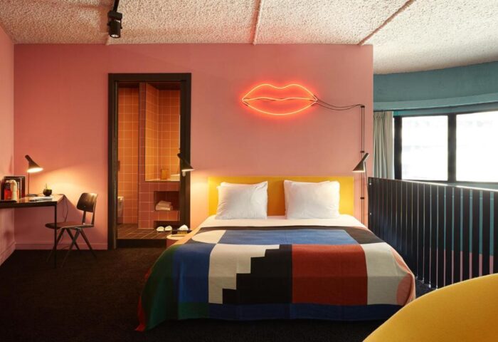 Gay-friendly The Student Hotel Amsterdam City room. Modern interior with neon lips decor, colorful bedspread, desk, and bathroom.