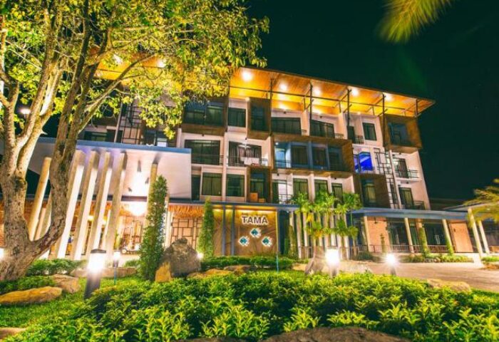 The Tama Hotel exterior at night. A gay-friendly hotel with modern architecture, lush landscaping, and warm lighting. Ideal for gay travel and vacations.