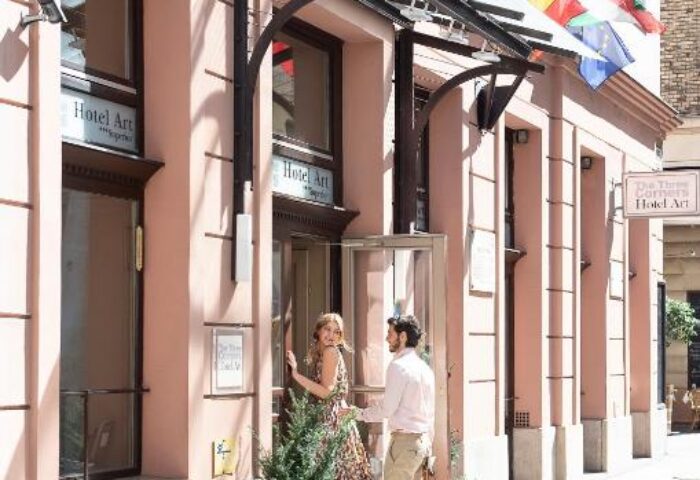 The Three Corners Hotel Art Superior entrance. Gay-friendly hotel with couple entering. Flags, pink facade, and Hotel Art sign visible.