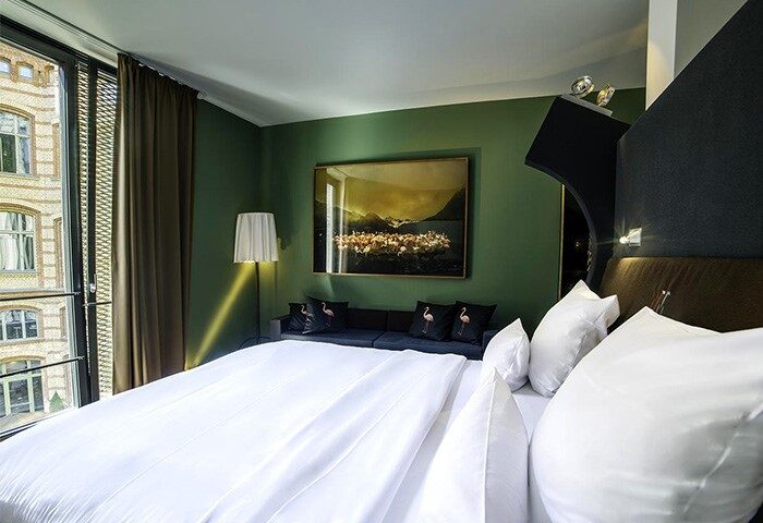 The Weinmeister Berlin-Mitte Adults Only hotel room. Gay-friendly, pet-friendly hotel with a view, bed, couch, and flamingo pillows.