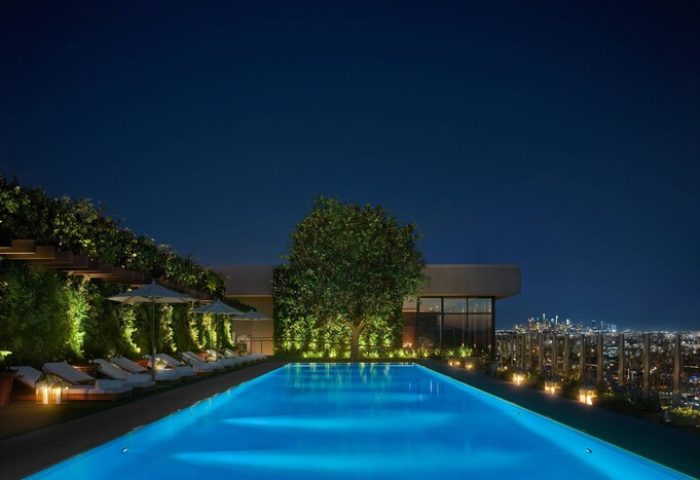 Night view of The West Hollywood EDITION, a gay-friendly hotel. Lit pool, lounge chairs, and city skyline. Luxury travel for gay men.