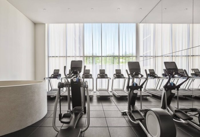 Gym at The West Hollywood EDITION, a gay-friendly hotel. Treadmills and elliptical machines face a large window. Fitness for gay men.