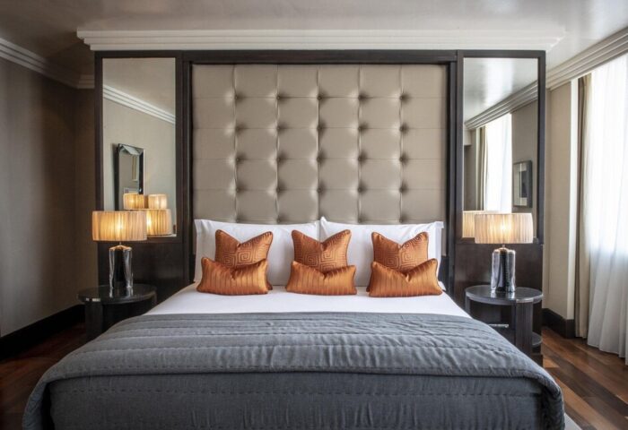 The Westbury Hotel's gay-friendly room: King bed with a tufted headboard, orange pillows, gray quilt, and mirrored side panels. Upscale design.