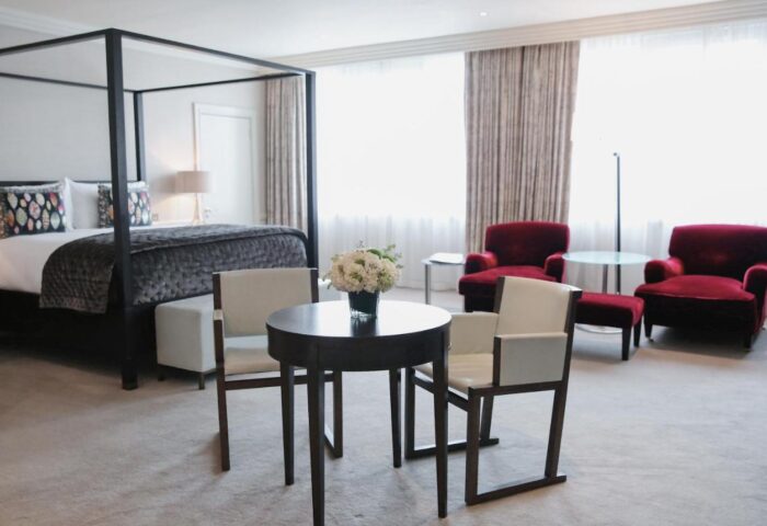Gay-friendly The Westbury Hotel room. Features a four-poster bed, table, chairs, and red armchairs. Great for gay men travel advice.