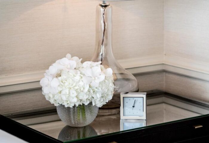 Nightstand detail at The Westbury Hotel, a gay-friendly hotel. Features a lamp, flowers, and clock, reflecting luxury and comfort.