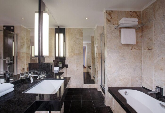 Bathroom at The Westin Grand Frankfurt, a gay-friendly hotel. Features marble tile, black granite counters, tub, and shower for a luxurious stay.