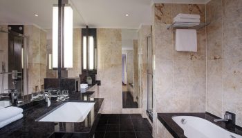 Bathroom at The Westin Grand Frankfurt, a gay-friendly hotel. Features marble tile, black granite counters, tub, and shower for a luxurious stay.