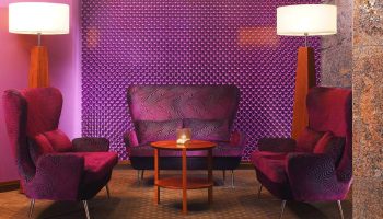 The Westin Grand Frankfurt gay-friendly hotel lounge area. Purple chairs and textured wall, lamps, and table create a stylish, modern space.
