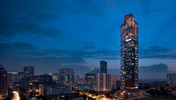 Night view of The Westin Jakarta, a gay-friendly hotel. The Jakarta skyline features illuminated skyscrapers against a dark blue sky.
